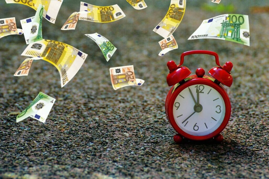 Wecker steht auf dem Boden und Geldscheine fallen vom Himmel als Symbol für den Zeitwert bei Optionen